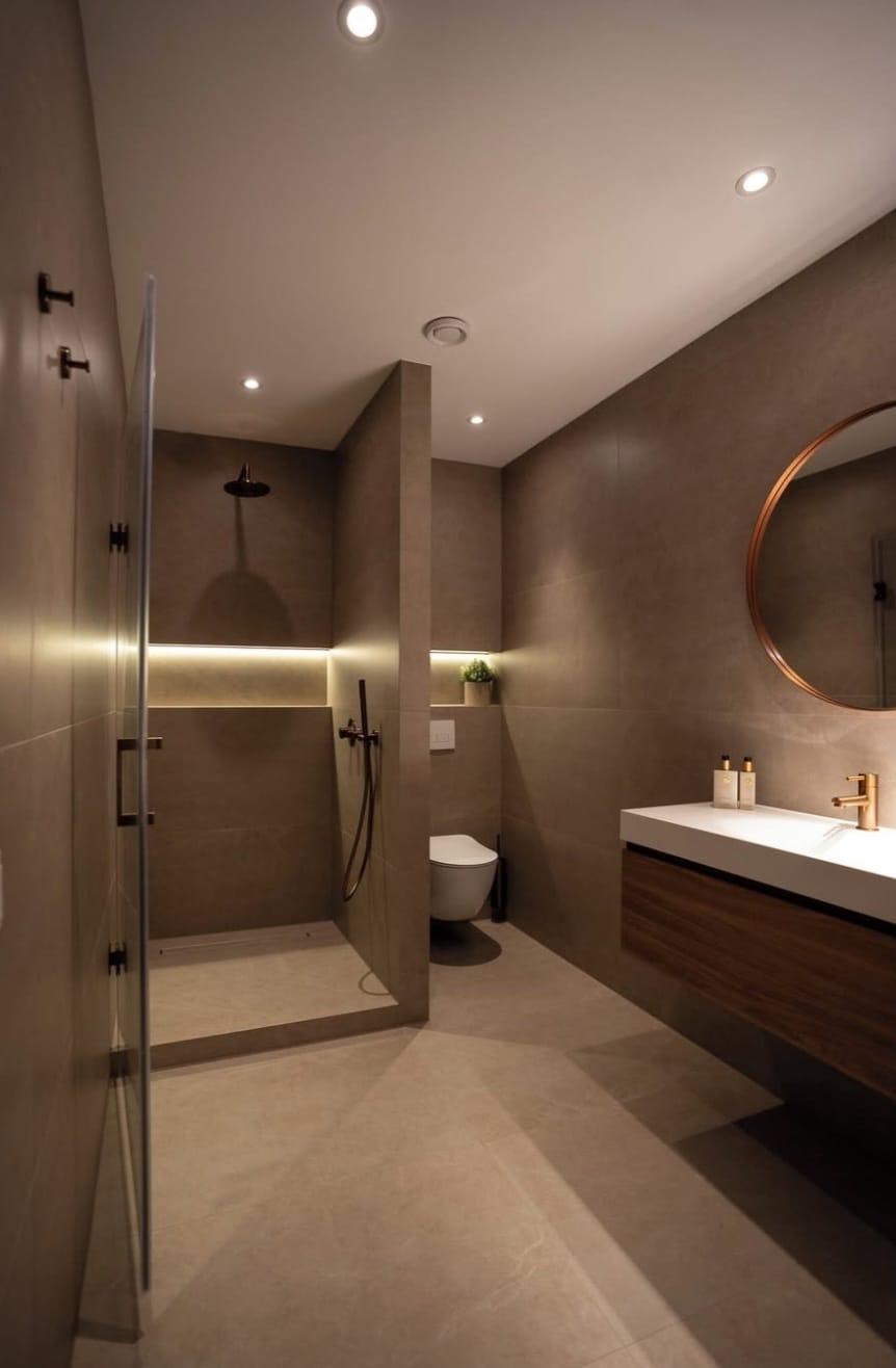 Walk-in douche met taupe natuursteen, walnut vanity en LED-strip verlichting